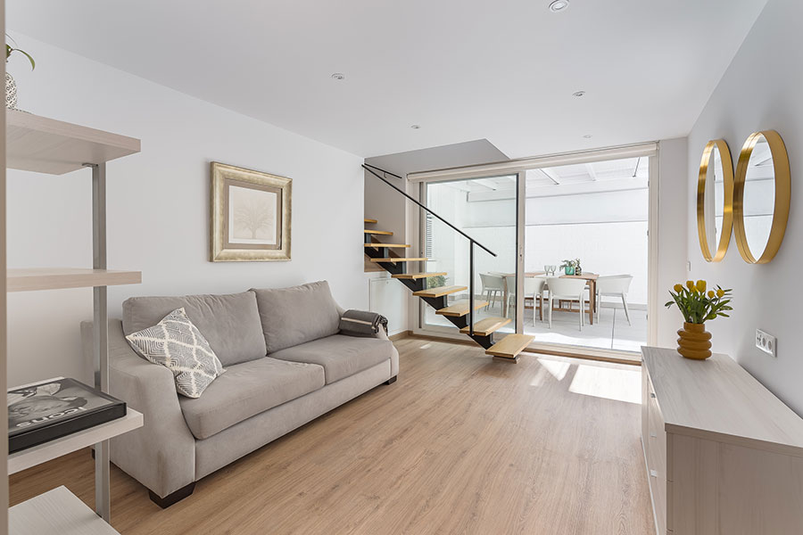 Vista del salón con la escalera de madera y patio al fondo del piso dúplex de 4 habitaciones de alquiler en Cuatro Caminos, Madrid.