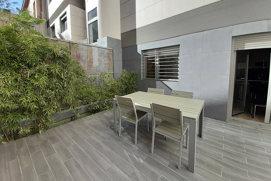 Terraza moderna en planta baja de un edificio en Madrid, con mobiliario exterior minimalista, suelo cerámico gris y vegetación que aporta privacidad, ideal para relajarse o socializar al aire libre.